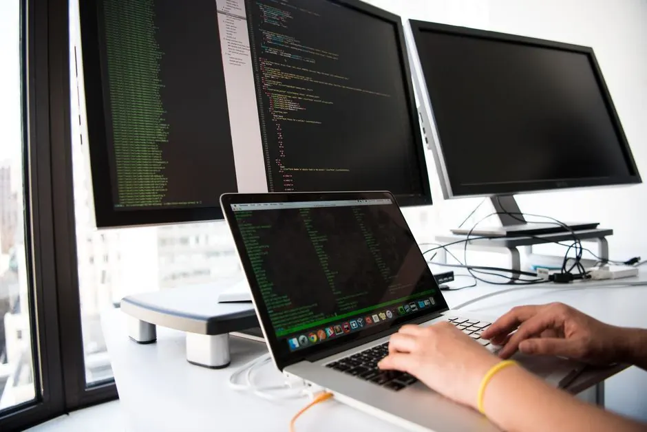 Hands typing code on a laptop in front of monitors
